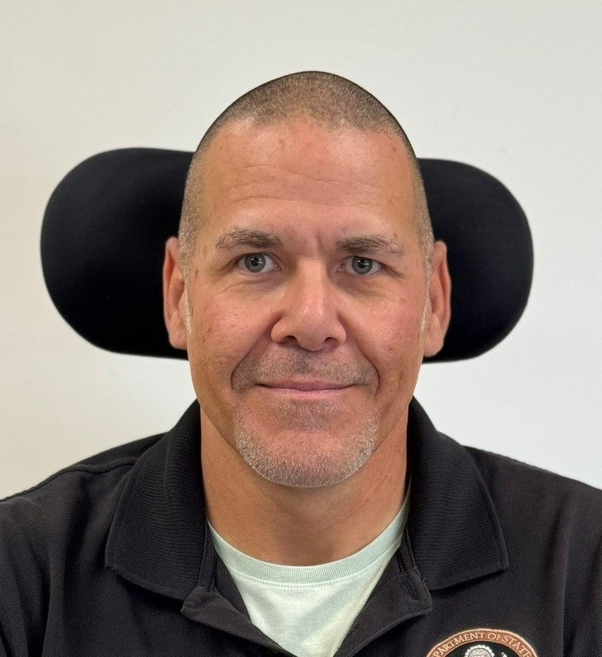  Photo of a man sitting in a wheelchair against an off-white background.