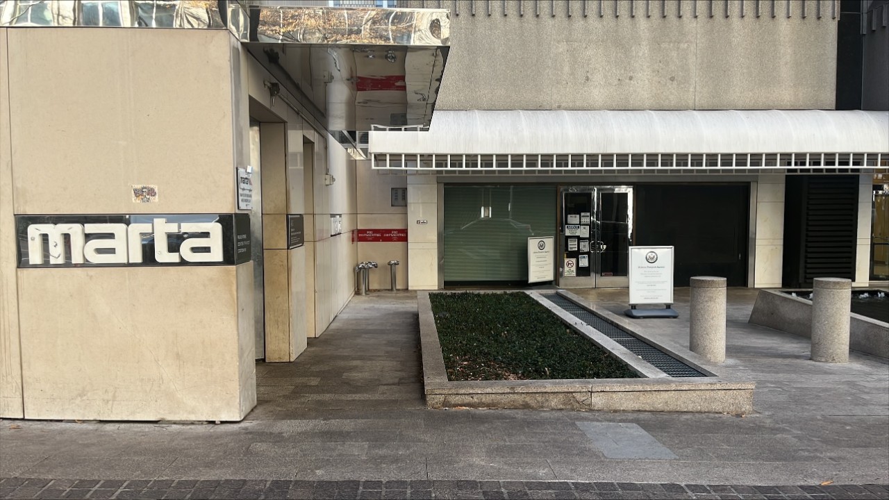 Exterior of Atlanta Passport Agency. The building is next to a MARTA sign on the side of the building. Concrete bollards and a sign are in front of the entrance. 