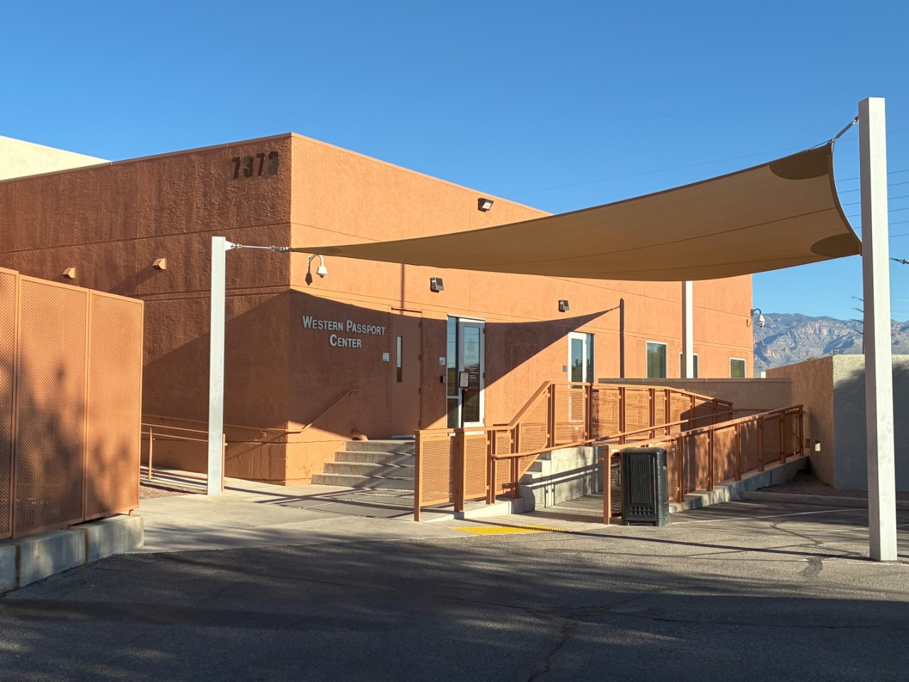 Exterior of Western Passport Center. It is in a short stucco building with a shade sail over the front entrance.